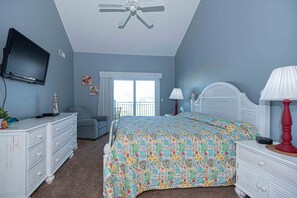 Une chambre à coucher comprenant un lit, une commode, un téléviseur, un ventilateur de plafond, une fenêtre et une lampe.