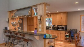 A modern kitchen with wooden cabinets, a bar area with stools, and a dining table with chairs. - Hot Tub | Deck | Fire Pit | BBQ | 2 Living Rooms (Incline Village)
