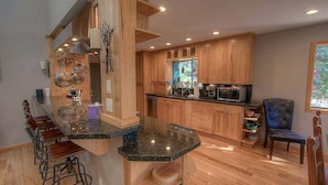 A kitchen with wooden cabinets, a granite countertop, and a bar area with stools. - Hot Tub | Deck | Fire Pit | BBQ | 2 Living Rooms (Incline Village)