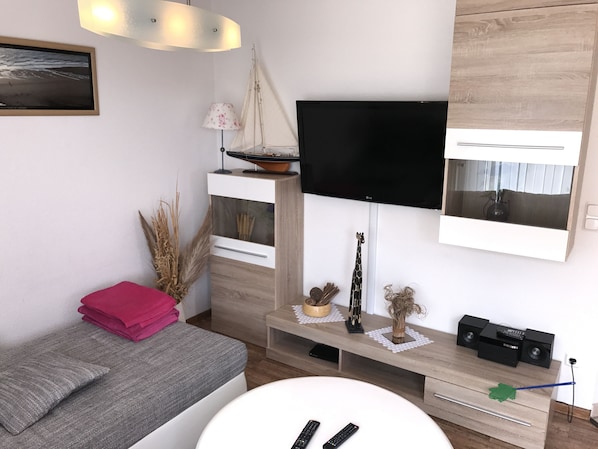 Un salon moderne avec un téléviseur à écran plat fixé au mur, une petite maquette de voilier et une figurine de girafe décorative.