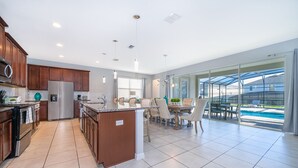 A modern kitchen with a central island, stainless steel appliances, and a dining area with a glass door leading to a pool. - GB1737 Home 5/5 Private Pool & Jaccuzi, Free Waterpark (Kissimmee)