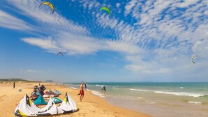 Une plage avec des tentes et des gens, et des cerfs-volants qui volent dans le ciel.