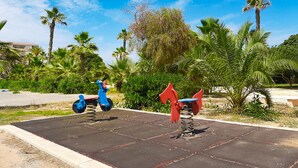 Deux balançoires sur une aire de jeux dans un parc, avec des palmiers et un ciel dégagé.