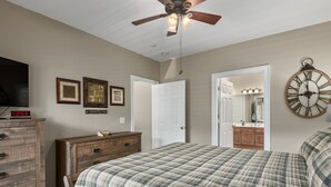 A bedroom with a bed, dresser, television, ceiling fan, and a door leading to a bathroom. - 3's a Birdie - 2BR, 2BA Condo, Golf & Mountain View (Maggie Valley)