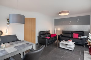 Ein modernes Wohnzimmer mit einer Couch, Sesseln, einem Couchtisch und einem Essbereich.