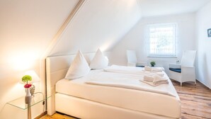 Ein modernes Schlafzimmer in Weiß mit einem Bett, Kissen, einem Nachttisch und einem Sessel.