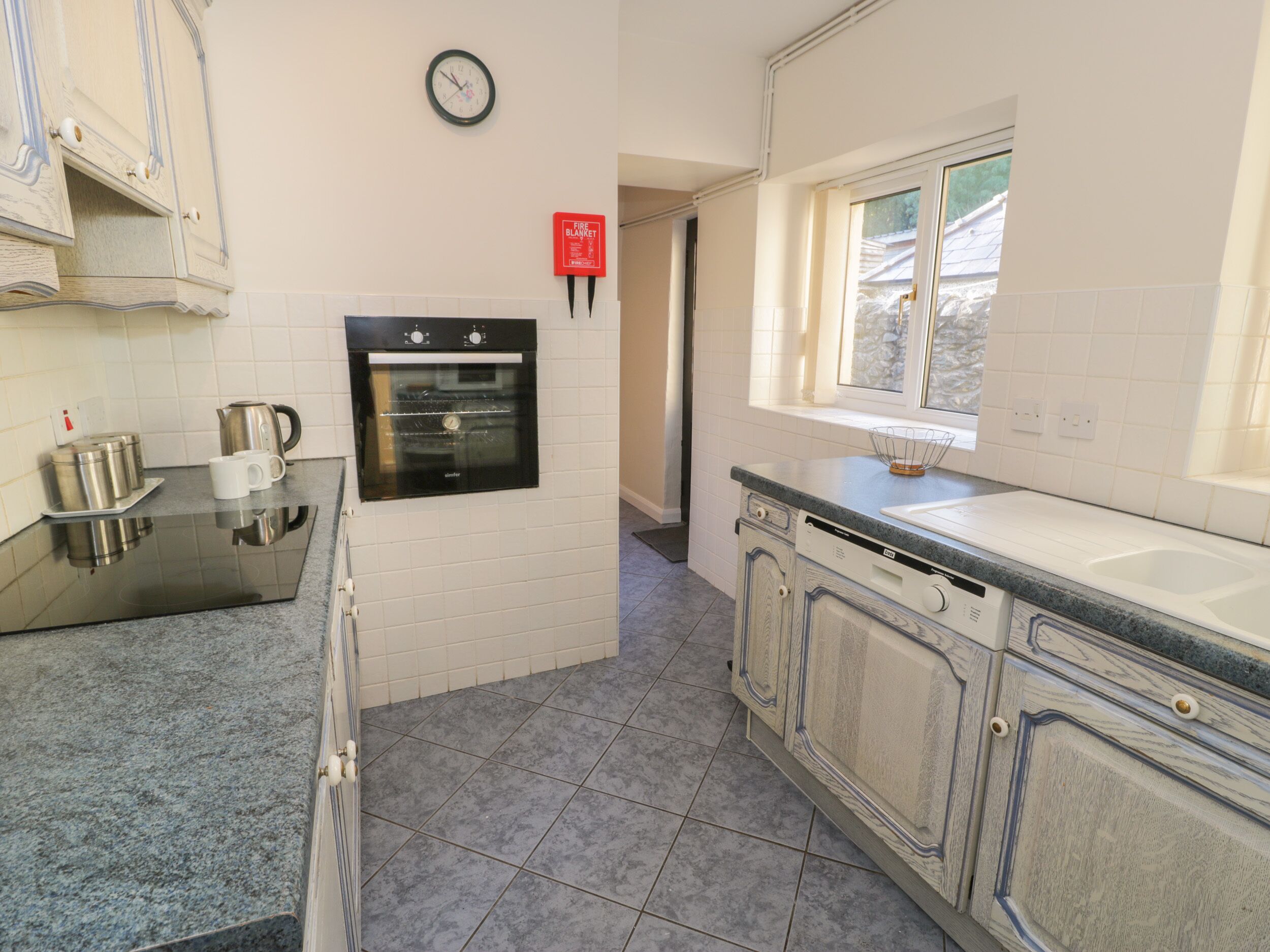 Una cocina con armarios blancos, horno integrado, cafetera y ventana.