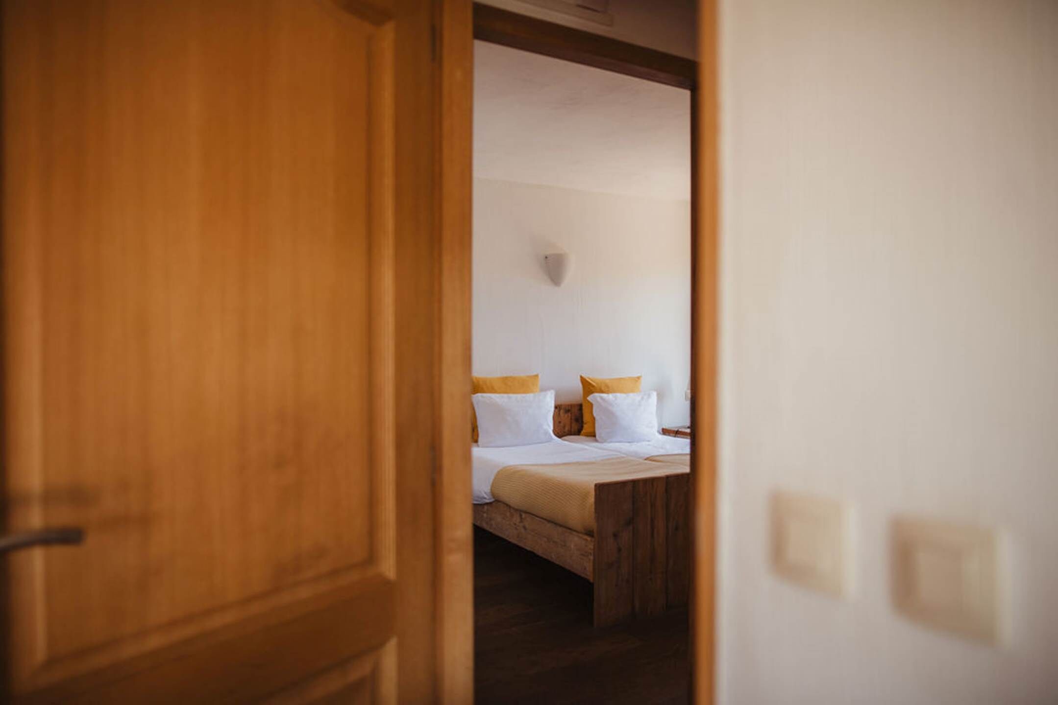 Een slaapkamer met een houten bed, witte en gele kussens en een houten deur.
