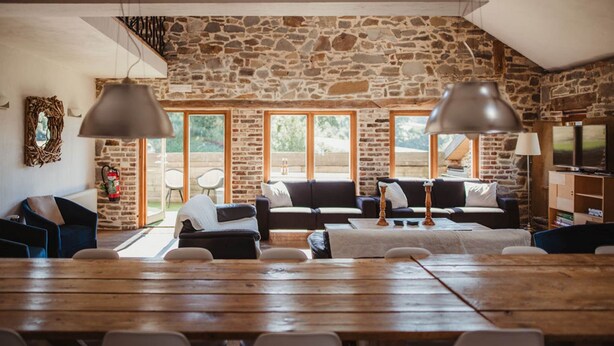 Ein rustikaler Innenraum mit Steinwänden, einem Holzespeisebereich und einer gemütlichen Sitzecke mit Sofas und Lampen.
