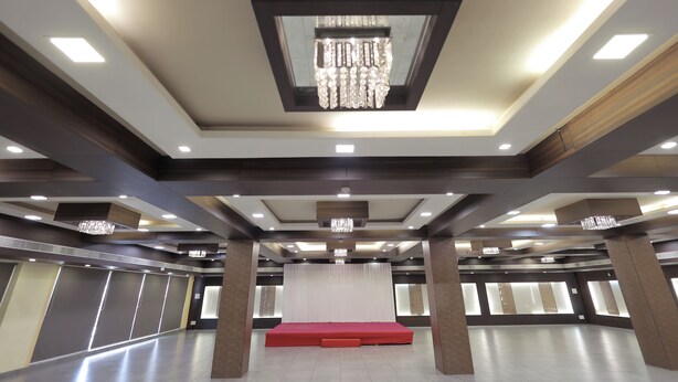 A spacious hall with a central stage, recessed lighting, and a chandelier. - HOTEL SHAGUN ROOMS & BANQUET Surat (Surat)