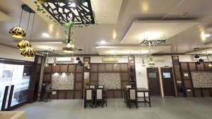A restaurant with a modern interior, featuring a dining area with tables and chairs, decorative hanging lights, and a patterned wall design. - HOTEL SHAGUN ROOMS & BANQUET Surat (Surat)