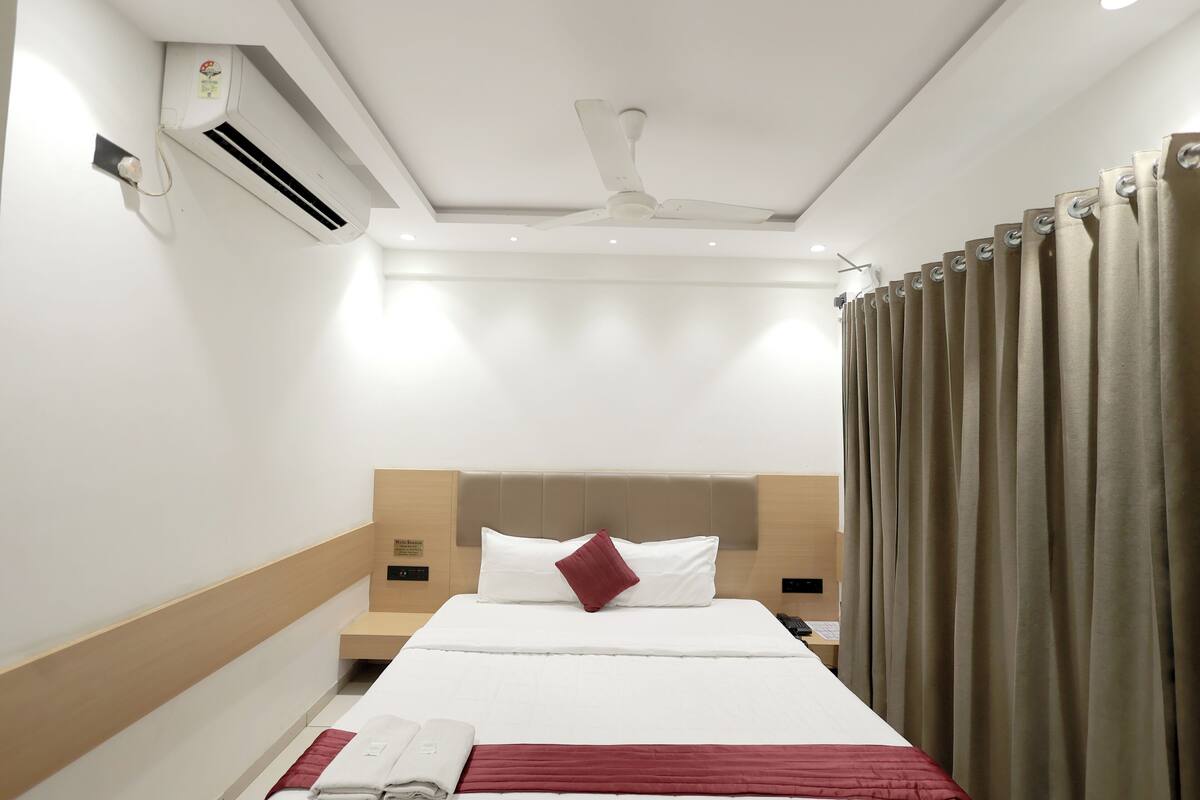 Een hotelkamer met een bed, een airconditioning, een plafondventilator en gordijnen.