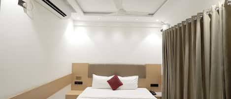 A hotel room with a bed, an air conditioning unit, a ceiling fan, and curtains.