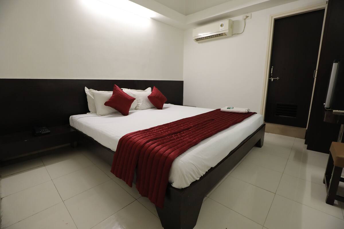 Een hotelkamer met een bed, nachtkastje, televisie en airconditioning.