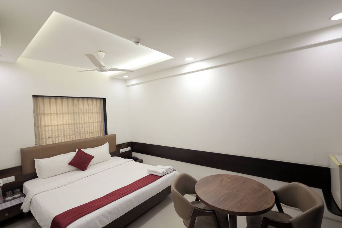 Een hotelkamer met een bed, een ronde houten tafel, een plafondventilator en een raam met gordijnen.