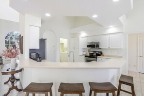 A modern kitchen with white cabinetry, a central island with stools, and recessed ceiling lights.