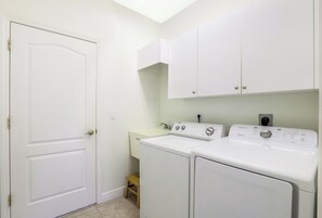 A laundry room with a white door, a washing machine, a dryer, and a small stool.