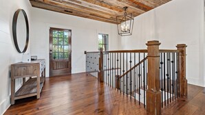 Un'ampia stanza con pavimento in parquet, una scala in legno con ringhiere nere e un grande specchio a parete.