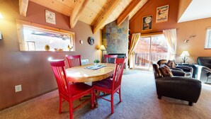 Una habitación acogedora con una mesa de comedor de madera, sillas rojas, un sofá de cuero negro y una chimenea de piedra.