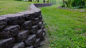 Un muro de piedra en un parque, con césped y árboles al fondo.