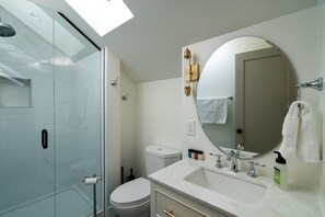 A modern bathroom with a glass shower enclosure, a white toilet, a large mirror, and a marble sink. - Guest House | Baker Neighborhood | Walk to Restaurants (Denver)