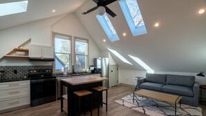 Eine moderne Küche mit einer zentralen Kochinsel, weißen Schränken und einem schwarzen Herd. Dachfenster und ein großes Fenster sorgen für natürliches Licht.