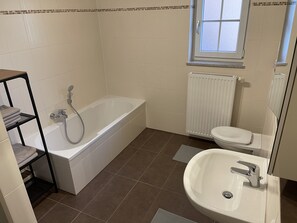 A bathroom with a bathtub, toilet, sink, and a window above the toilet. - Apartment Mühlbach (Bad Abbach)