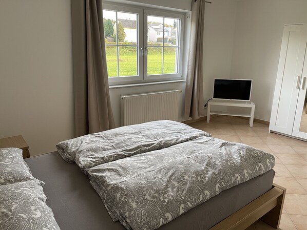 Quarto com duas camas, uma televisão sobre uma mesinha e um guarda-roupa.