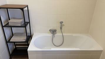 A bathroom with a white bathtub, a showerhead, and a black metal shelf with folded towels.
