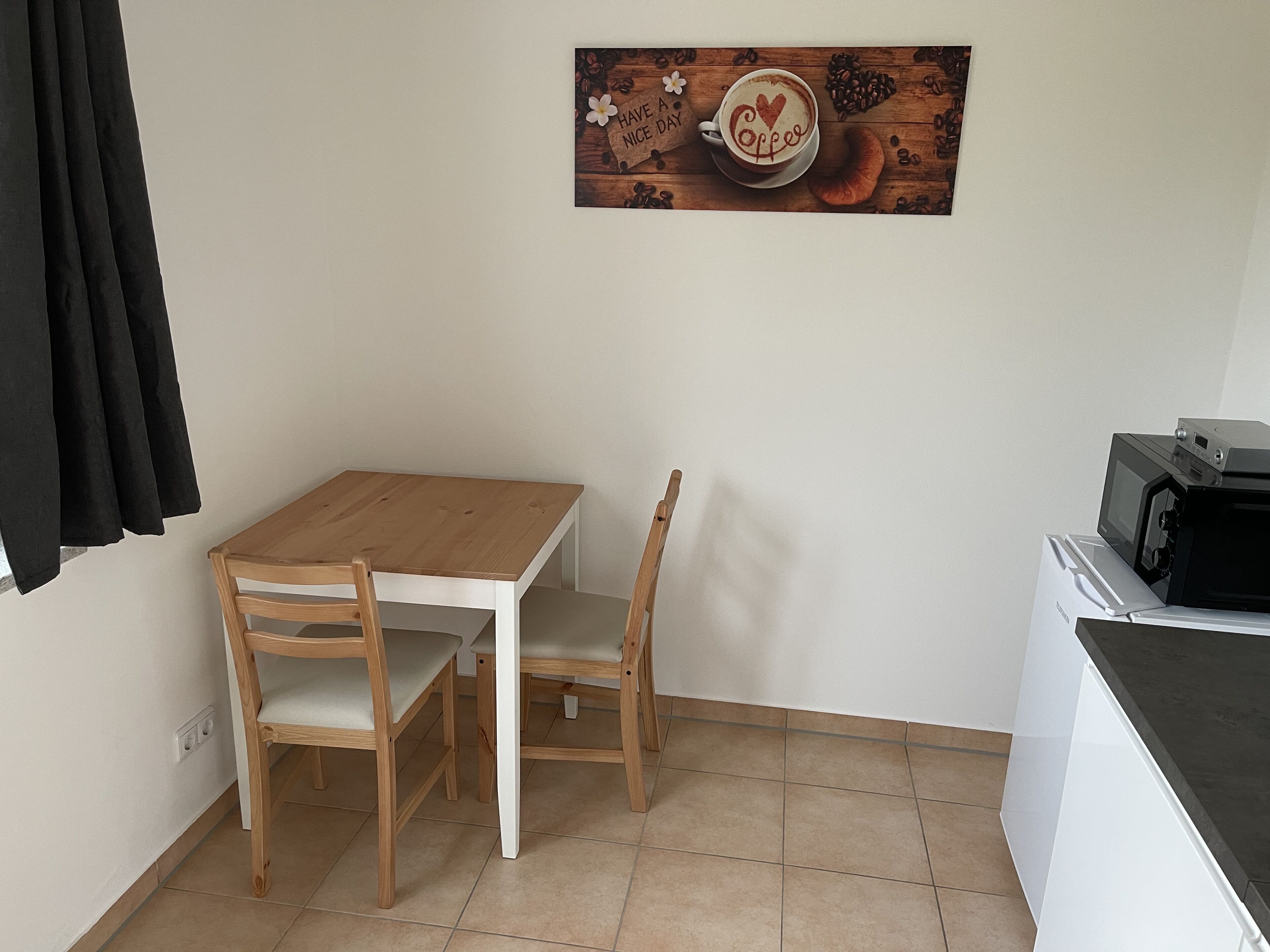 Una pequeña cocina con una mesa de madera y dos sillas, un microondas y una cafetera.