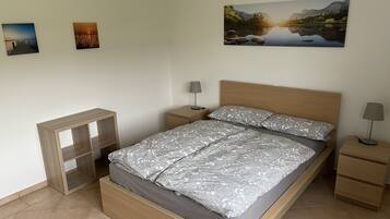 Un dormitorio con una cama de madera, una mesita de noche, un pequeño estante de madera y un cuadro de un paisaje en la pared.