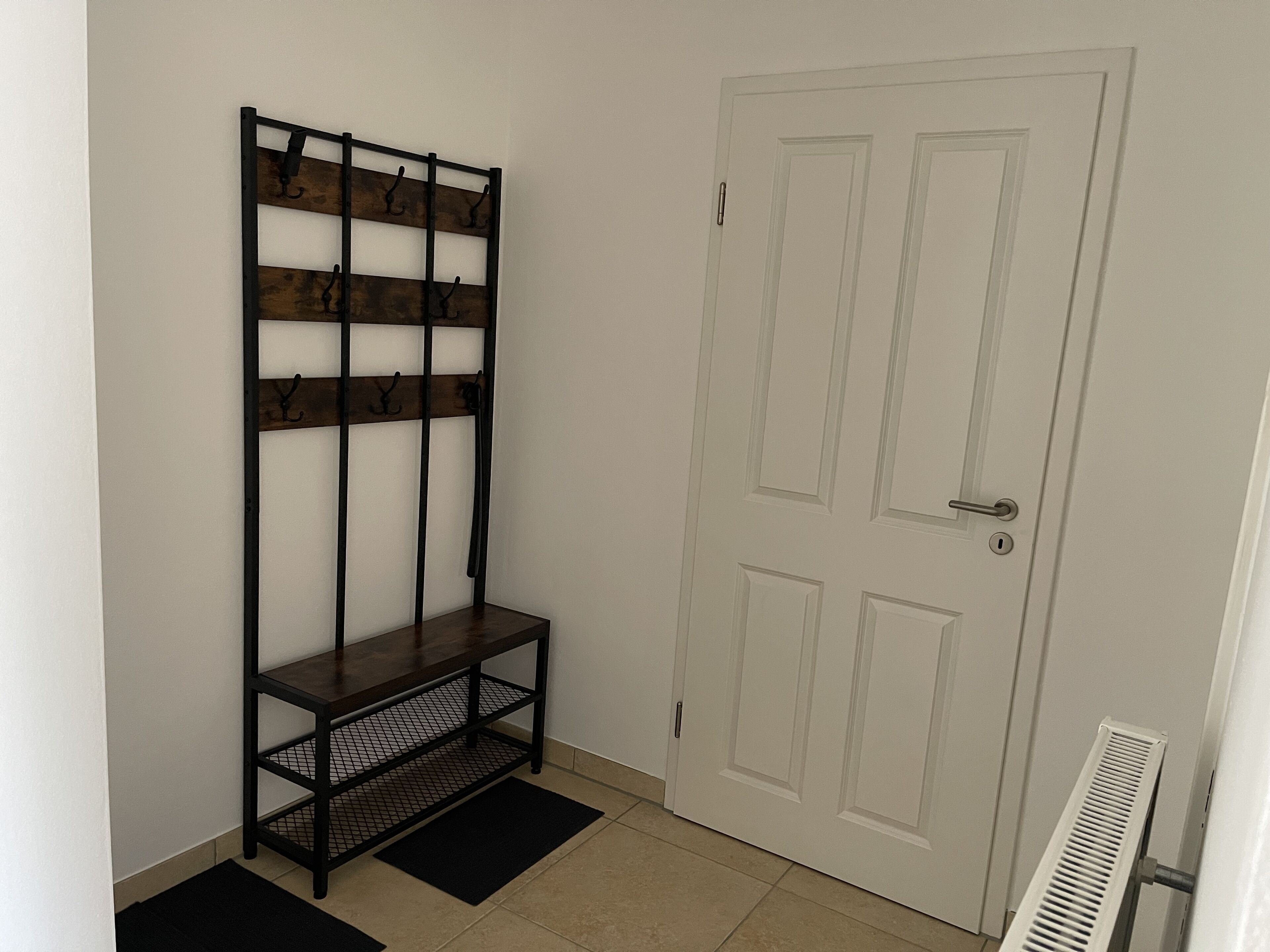A hallway with a wooden bench, a white door, and a radiator.