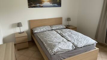 Une chambre à coucher avec un lit en bois, deux tables de chevet, une lampe sur chacune, et un tableau représentant un paysage accroché au mur.