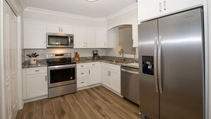 Une cuisine moderne avec des meubles blancs, des appareils électroménagers en acier inoxydable et un plancher en bois.