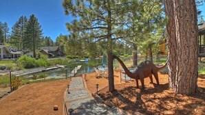En dinosauriestaty i en park med en damm, träd och en bro i bakgrunden.