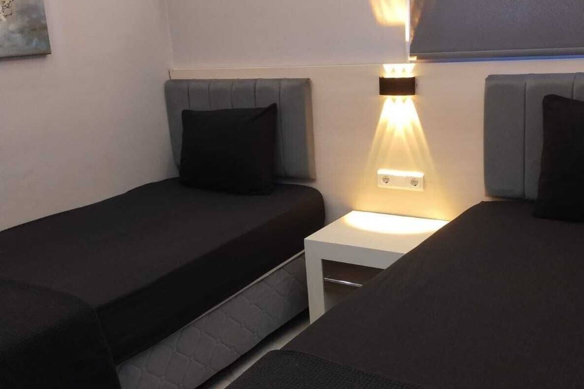 A bedroom with two single beds, a nightstand with a lamp, and an air conditioning unit mounted on the wall.