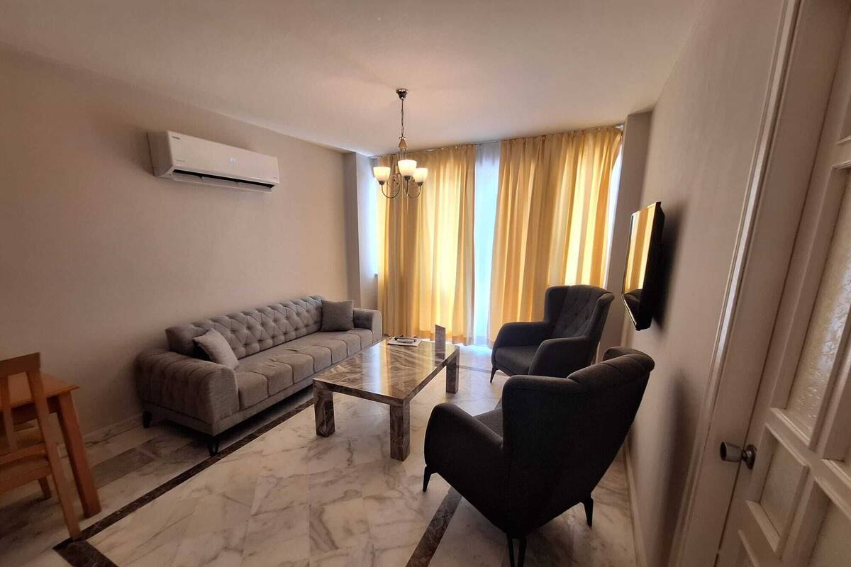 A living room with a sofa, armchairs, a coffee table, and a TV mounted on the wall.