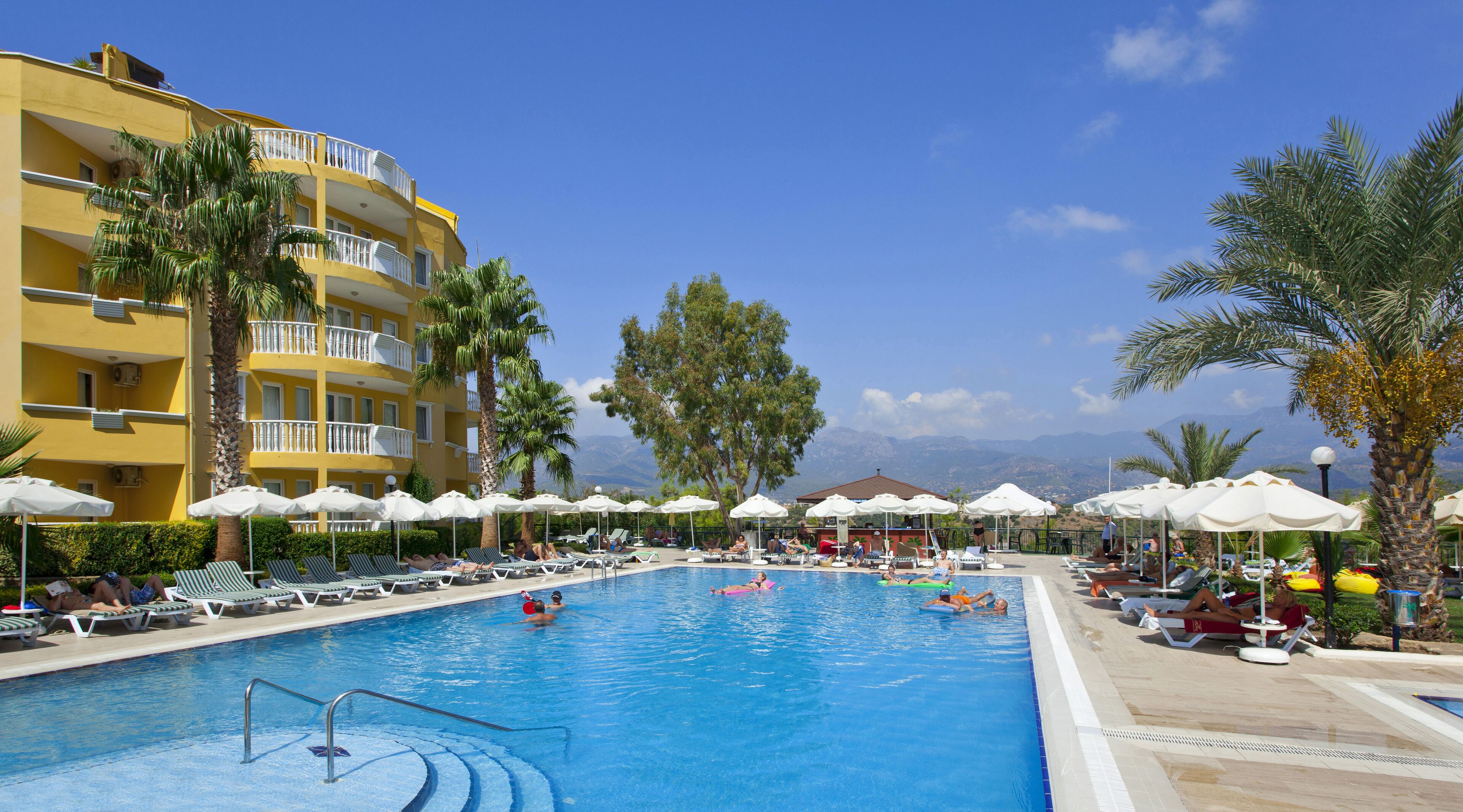A pool area with lounge chairs, umbrellas, and a view of mountains.