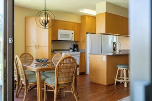 Una cocina compacta con armarios de madera, un microondas, un refrigerador y un comedor con sillas de mimbre y una mesa.
