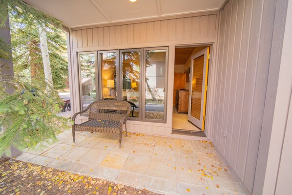 Relax in the covered outdoor seating area with a wicker bench, adjacent to the building's entrance.