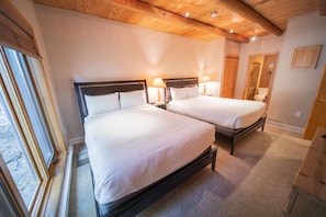 Two single beds with wooden headboards and white bedding, a wooden ceiling with exposed beams, and a dresser.