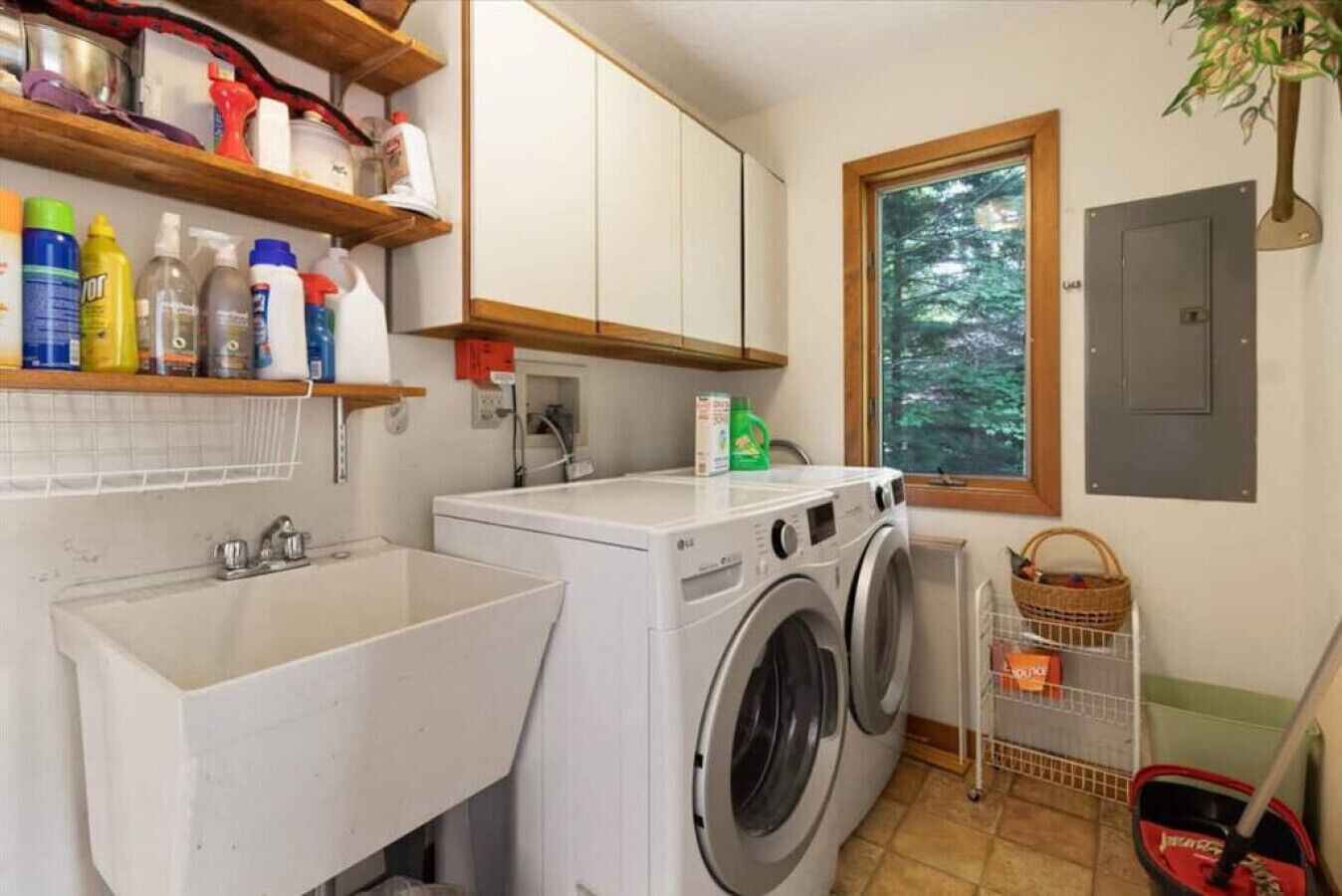 Un área de lavandería con lavadora, pileta y estantes con productos de limpieza.
