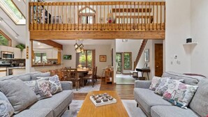 A spacious living area with a high ceiling and a wooden balcony, furnished with sofas and a coffee table. - Pocono Pines Family Retreat: Game Room, Sunroom & Pets Welcome! (Pocono Pines)