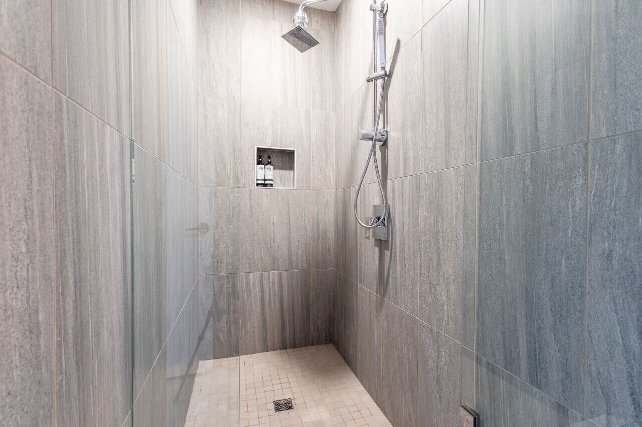 A modern shower with a handheld showerhead and a wall-mounted faucet.