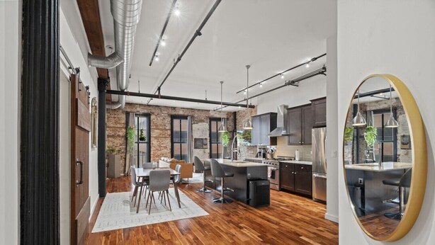 A modern kitchen with a central island, wooden flooring, and a large mirror.