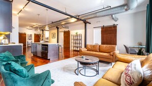 A spacious living area with a sofa, chairs, and a coffee table. There is a kitchen area in the background with a dining table and chairs.