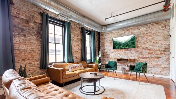 A living room with a brick wall, leather sofas, a round coffee table, and a TV mounted on the wall.