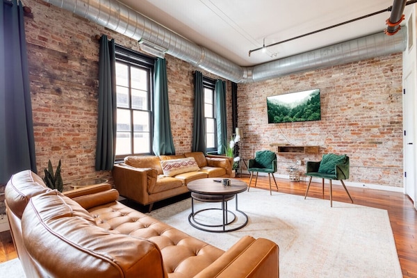 Open-concept living room with exposed brick and large windows