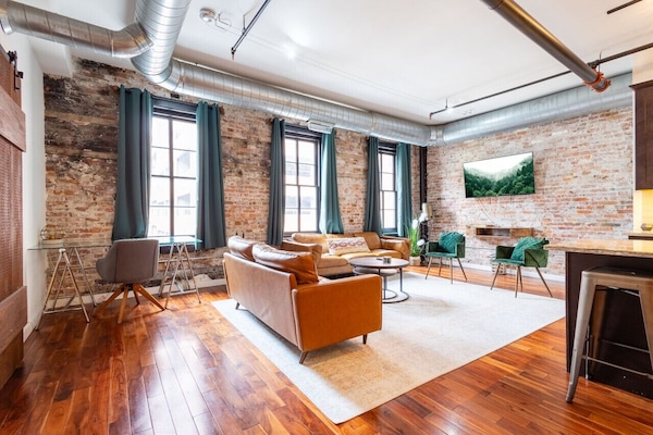 Open-concept living and dining area with exposed brick and large windows
