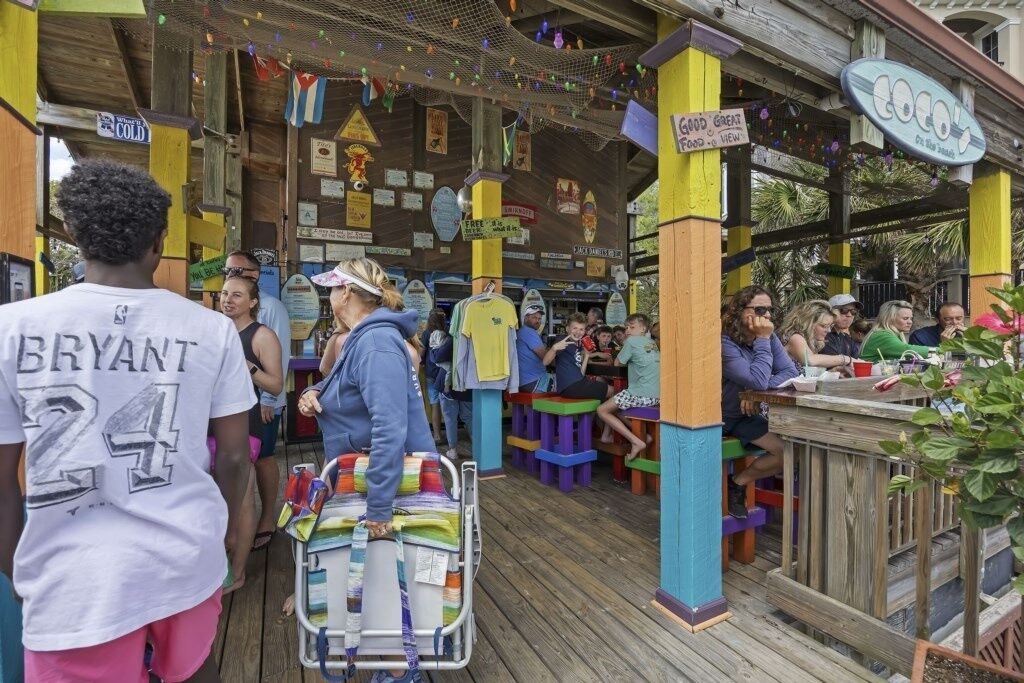 Un espacio de estar al aire libre techado con taburetes coloridos y una terraza de madera.